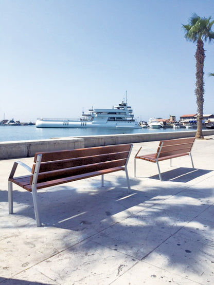 Zwei Parkbänke an einer Promenade mit Palme und mit Blick auf den Hafen und eine große Yacht