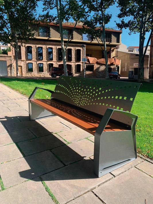 Eine elegante Parkbank mit Sitzfläche aus Holz und Rückenlehne und Armlehne aus Metall mit Muster in einem Park